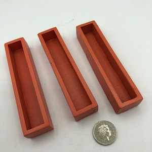May include: Three terracotta-coloured rectangular planters, each with a shallow trough, are arranged in a row. A British one-pound coin is placed below the planters for scale.
