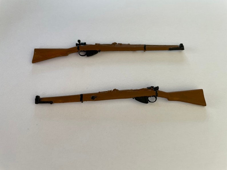 May include: Two miniature brown rifles with black details are displayed against a white background. The rifles have a classic design, with a wooden stock and a long barrel. The rifles are positioned parallel to each other.