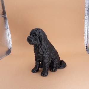 May include: Black figurine of a dog sitting with its head tilted to the side. The dog has a shaggy coat and is made of a smooth, matte material.