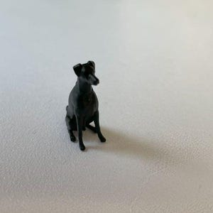 May include: A black miniature dog figurine sitting with its head turned to the side.