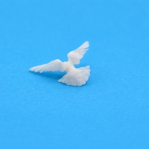 May include: A miniature white dove ornament with its wings spread, positioned on a vibrant blue backdrop. The dove's feathers are finely detailed. The image has a clean, minimalist style, with the dove as the central focus.