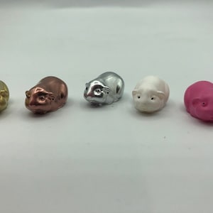 May include: Five small ceramic figurines of guinea pigs in different colours: gold, copper, silver, white and pink.