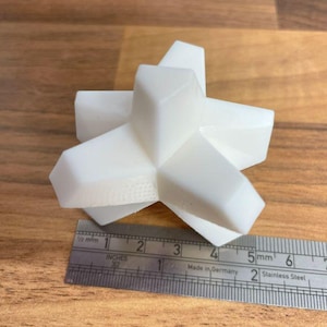 May include: A white, geometric, 3D printed object with a star-like shape. The object is about 2 inches wide and is sitting on a wooden surface.