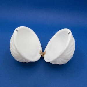 May include: A white ceramic hinged trinket box shaped like a seashell. The box is open, revealing the empty interior.