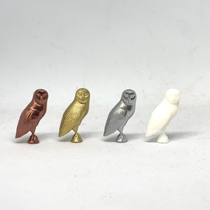 May include: Four ceramic owl figurines in different colors: copper, gold, silver, and white. The owls are all facing forward with their wings spread out.
