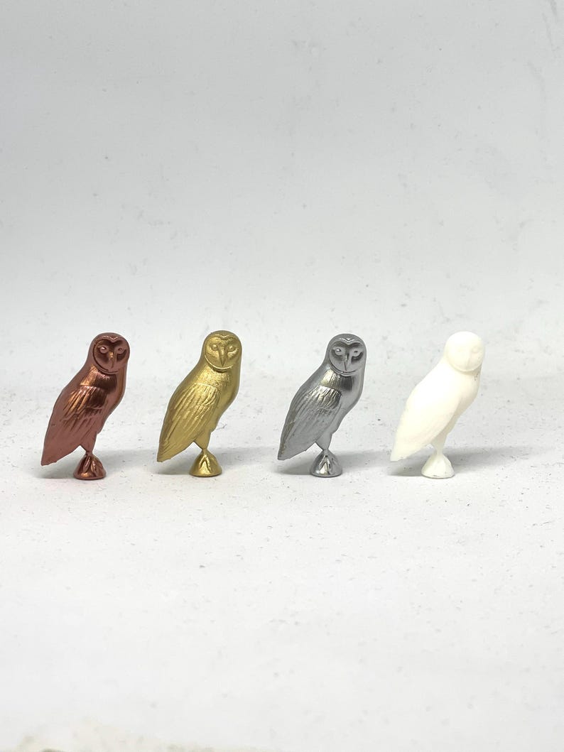 May include: Four ceramic owl figurines in different colors: copper, gold, silver, and white. The owls are all facing forward with their wings spread out.