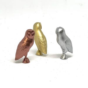 May include: Three small owl figurines, one in copper, one in gold, and one in silver.