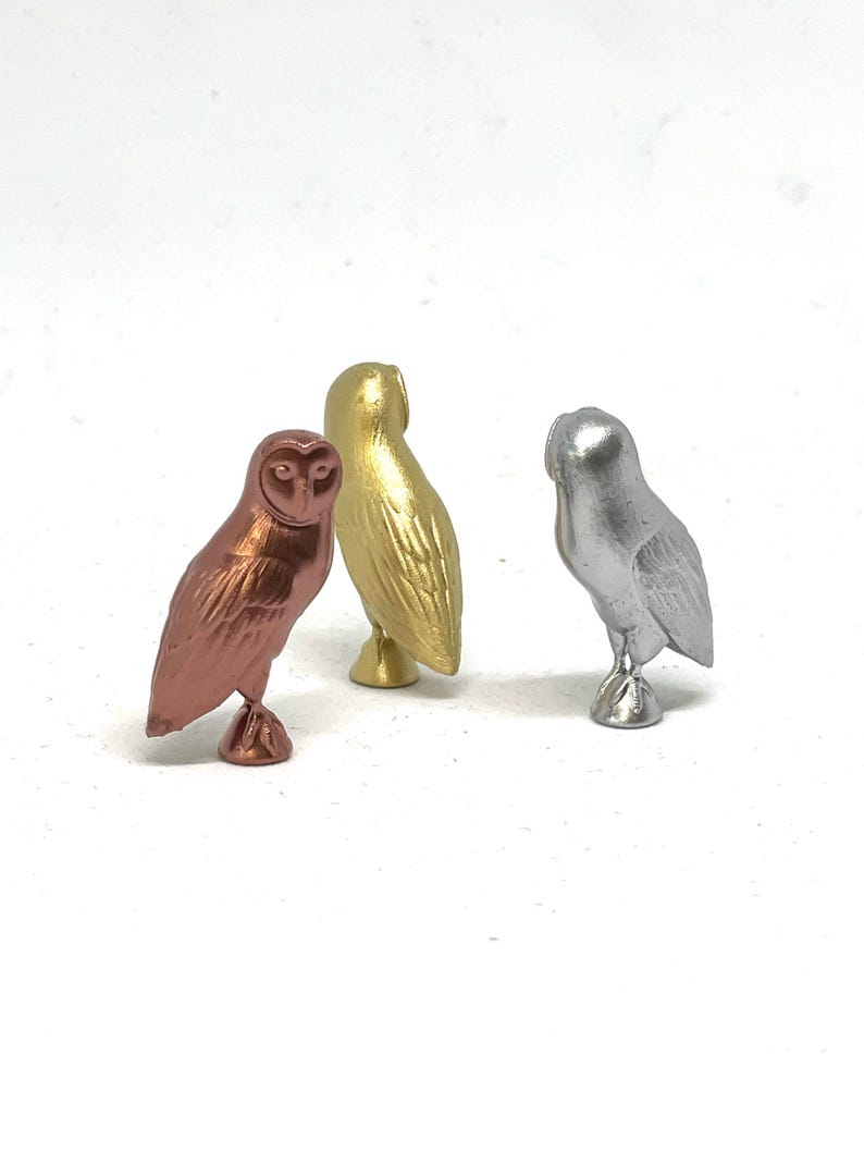 May include: Three small owl figurines, one in copper, one in gold, and one in silver.