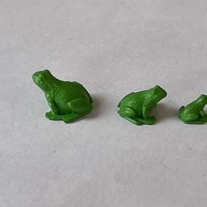 May include: Three green frog figurines of varying sizes. The largest frog is sitting with its legs outstretched, while the two smaller frogs are sitting with their legs tucked underneath them.