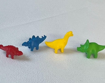 May include: Four small plastic dinosaur figurines in different colors: red, blue, yellow, and green. The dinosaurs are all facing the same direction.