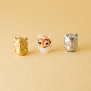 May include: Three small owl figurines, one gold, one white and one silver. The owls are all facing forward with their eyes closed.