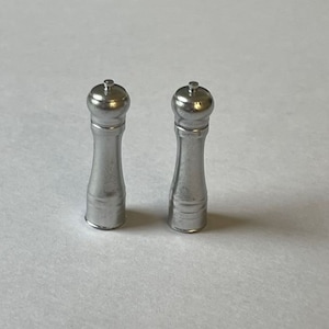 May include: Two silver pepper mills with a round top and a cylindrical body.