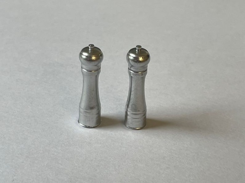 May include: Two silver pepper mills with a round top and a cylindrical body.