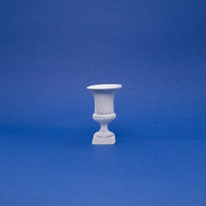 May include: A white ceramic planter with a fluted design and a round base. The planter is on a blue background.