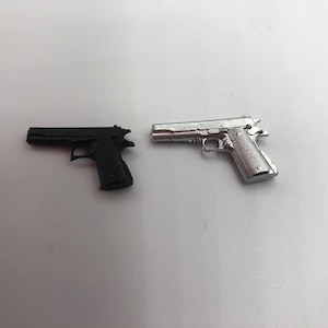 May include: Two toy pistols, one black and one silver, are shown on a white surface.