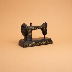 May include: Black metal sewing machine figurine with gold accents and the word "SINGER" on the side.