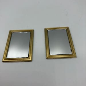 May include: Two gold-framed mirrors with a simple design. The mirrors are rectangular and have a smooth, reflective surface.