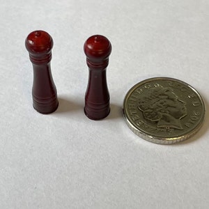 May include: Two small, dark red wooden salt and pepper shakers. The shakers are about the size of a British one pound coin.