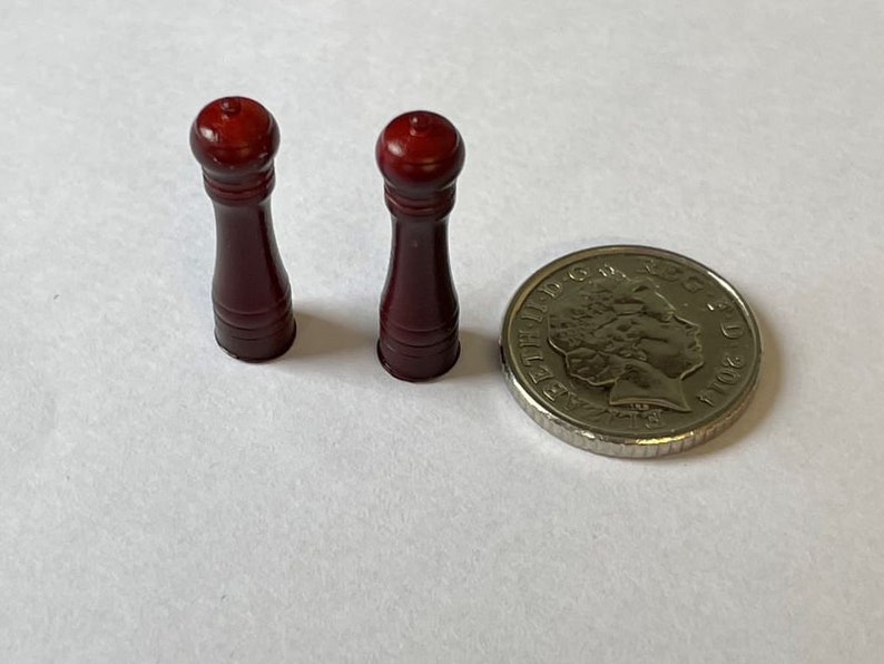 May include: Two small, dark red wooden salt and pepper shakers. The shakers are about the size of a British one pound coin.