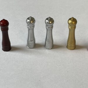 May include: Five salt and pepper shakers in different colors: red, silver, gold, and copper. The shakers are all the same size and shape, with a round top and a cylindrical body.