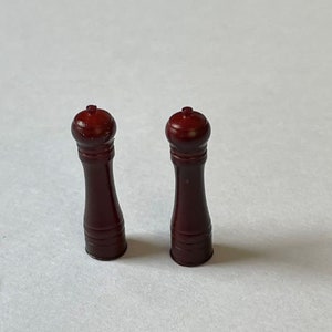 May include: Two wooden salt and pepper shakers with a dark brown finish. The shakers have a round top and a cylindrical body.