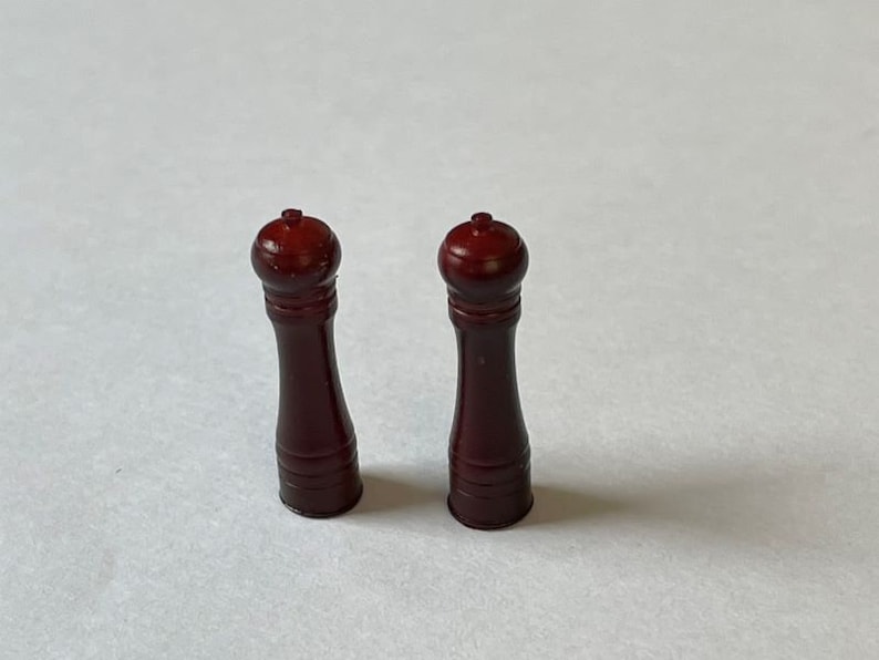May include: Two wooden salt and pepper shakers with a dark brown finish. The shakers have a round top and a cylindrical body.