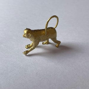 May include: A gold monkey figurine with a ring on its tail. The monkey is in a walking pose with its head turned to the side.