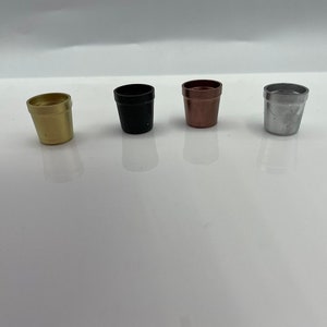 May include: Four small metal containers in different colours: gold, black, copper, and silver. The containers are all the same size and shape, and they are arranged in a row.