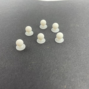 May include: Eight white plastic round buttons with a small raised sphere on top. The buttons are arranged in a triangular pattern on a grey surface.