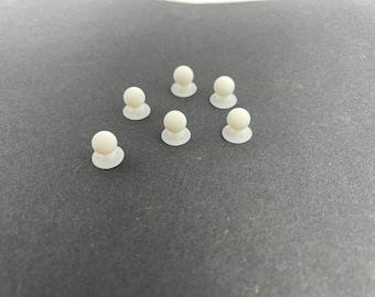 May include: Eight white plastic round buttons with a small raised sphere on top. The buttons are arranged in a triangular pattern on a gray surface.