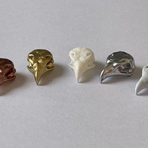 以下が含まれることがあります： 異なる色の小さな鳥の頭蓋骨の置物5つ。金色、銀色、白色、茶色の2色