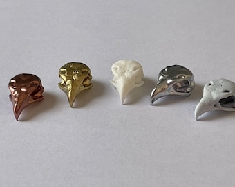 Könnte beinhalten: Fünf kleine Vogel-Schädel-Figuren in verschiedenen Farben: Gold, Silber, Weiß und zwei Brauntönen.