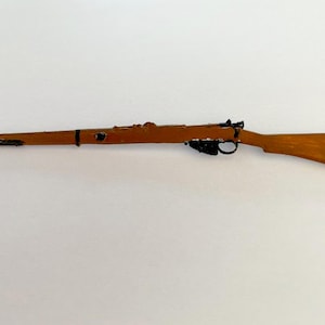 May include: A wooden toy rifle with a brown finish and black accents. The rifle features a trigger, a sight, and a stock. The toy rifle is a replica of a classic firearm.