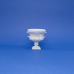 May include: White ceramic planter with ornate details and a pedestal base.