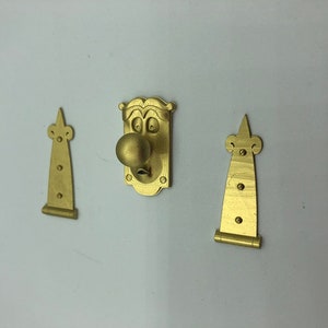 May include: A gold-coloured door handle with a face and a round knob. The handle is attached to two gold-coloured hinges.