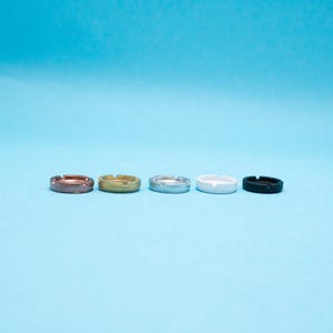 May include: Five small, round, metal rings in different colors: copper, gold, silver, white, and black.