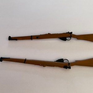 May include: Two miniature rifles with brown wooden stocks and black metal details are displayed against a white background. The rifles are positioned horizontally, showcasing their design and craftsmanship. The rifles are likely toy or model replicas.