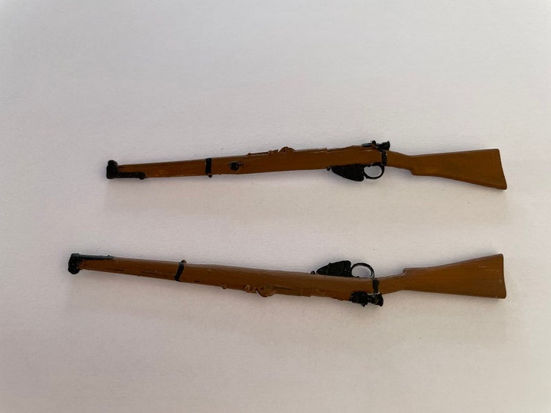 May include: Two miniature rifles with brown wooden stocks and black metal details are displayed against a white background. The rifles are positioned horizontally, showcasing their design and craftsmanship. The rifles are likely toy or model replicas.