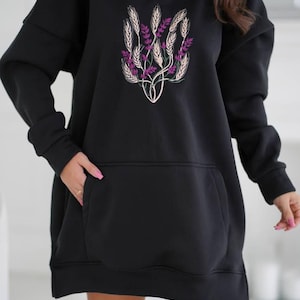 May include: Black oversized hoodie with a floral design featuring wheat and purple flowers. The hoodie has a large pocket on the front.