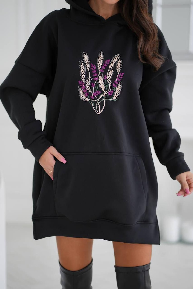 May include: Black oversized hoodie with a floral design featuring wheat and purple flowers. The hoodie has a large pocket on the front.