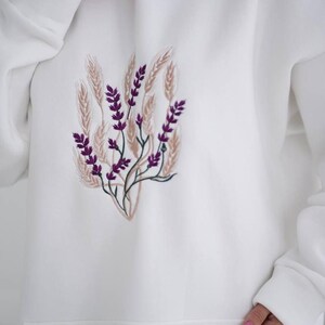 May include: White hooded sweatshirt with a purple and brown embroidered floral design.