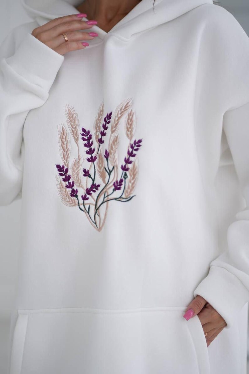 May include: White hooded sweatshirt with a purple and brown embroidered floral design.