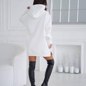 May include: A white oversized hoodie with a hood and a side slit. The hoodie is worn with black thigh-high boots.