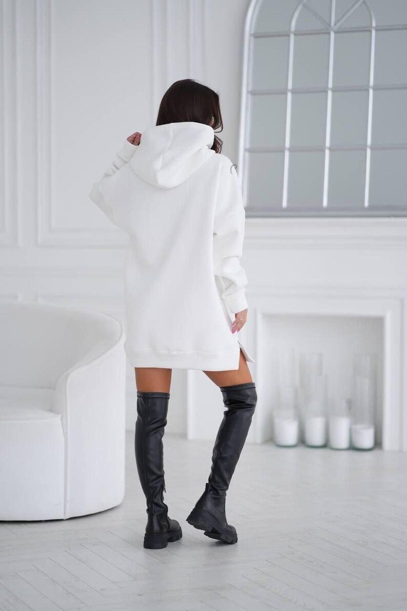 May include: A white oversized hoodie with a hood and a side slit. The hoodie is worn with black thigh-high boots.