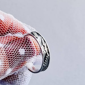 Könnte beinhalten: Ein silberner Ring mit einem detaillierten Design aus Blättern und Zweigen. Der Ring wird auf einem weißen Hintergrund gezeigt.