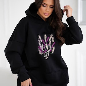 May include: Black oversized hoodie with a floral embroidery design featuring purple flowers and gold wheat stalks.