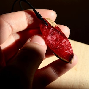 May include: A red and brown wood pendant with a resin inlay. The resin is a deep red colour with white swirls.
