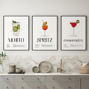 May include: Three framed wall art prints featuring minimalist line drawings of cocktails. The left print shows a Mojito with lime, the centre a Spritz with an orange slice, and the right a Cosmopolitan with a lime garnish, each with text.