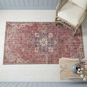 a large, intricately patterned rug on a wooden floor, with a wicker chair and a wooden coffee table nearby.
