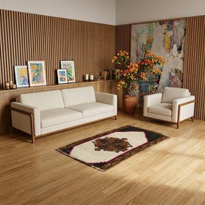 Puede incluir: Un salón con un sofá y un sillón color crema con marcos de madera. Una alfombra estampada descansa sobre el suelo de madera. Obras de arte y un gran arreglo floral añaden color. La habitación tiene una estética minimalista.